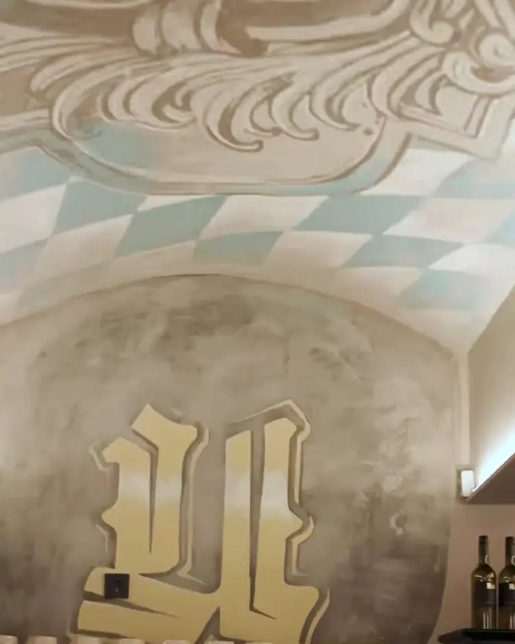 Das Kellergewölbe: gemalte Kartusche an der Decke, darunter das goldene Fraktur-U an der Wand und die Theke